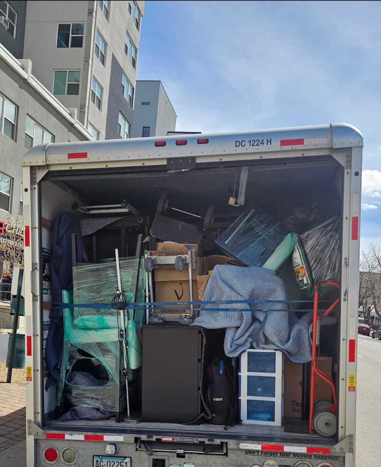 Box truck loaded floor-to-ceiling with furniture and boxes, parked at an apartment building
